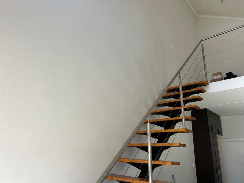 Modern open-tread staircase featuring timber steps, stainless steel balustrades, and wire cable railings, leading to an upper mezzanine level.