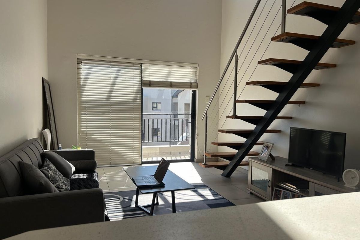A bright living room featuring a modern floating staircase with metal railings, tiled flooring, and a sliding glass door leading to a balcony.