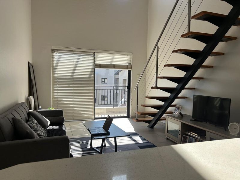 A bright living room featuring a modern floating staircase with metal railings, tiled flooring, and a sliding glass door leading to a balcony.