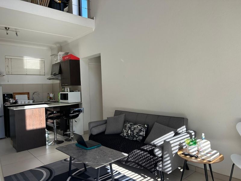 Open plan living area featuring a compact kitchen with dark cabinetry, tiled floors, and a mezzanine level with a metal railing.