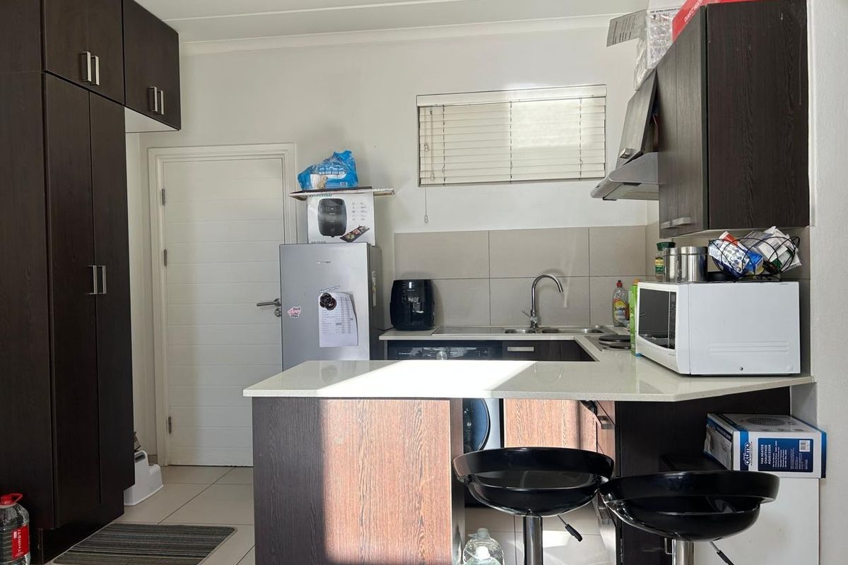 Compact kitchen featuring dark wood cabinetry, stone countertops, a tiled backsplash, and an integrated extractor fan with a breakfast bar area.