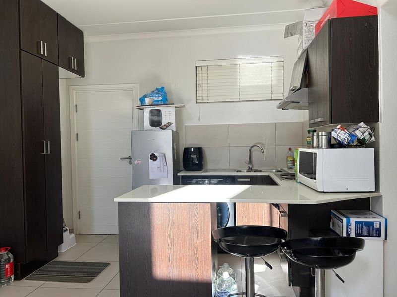 Compact kitchen featuring dark wood cabinetry, stone countertops, a tiled backsplash, and an integrated extractor fan with a breakfast bar area.