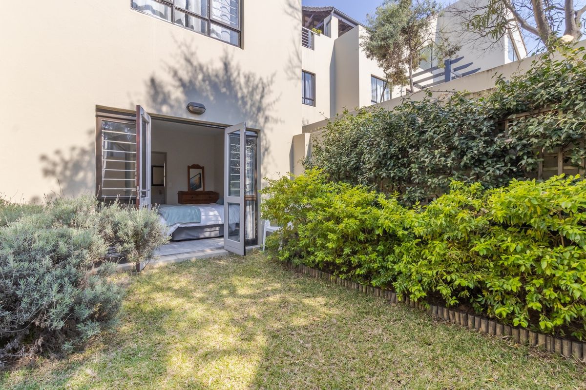 A private rear garden featuring a small lawn, established hedging, and direct access to the interior via double french doors with security gates.