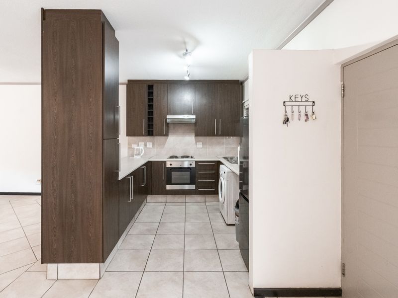 A functional kitchen featuring dark wood cabinetry, built-in oven, hob, extractor fan, and tiled flooring with a neutral backsplash.