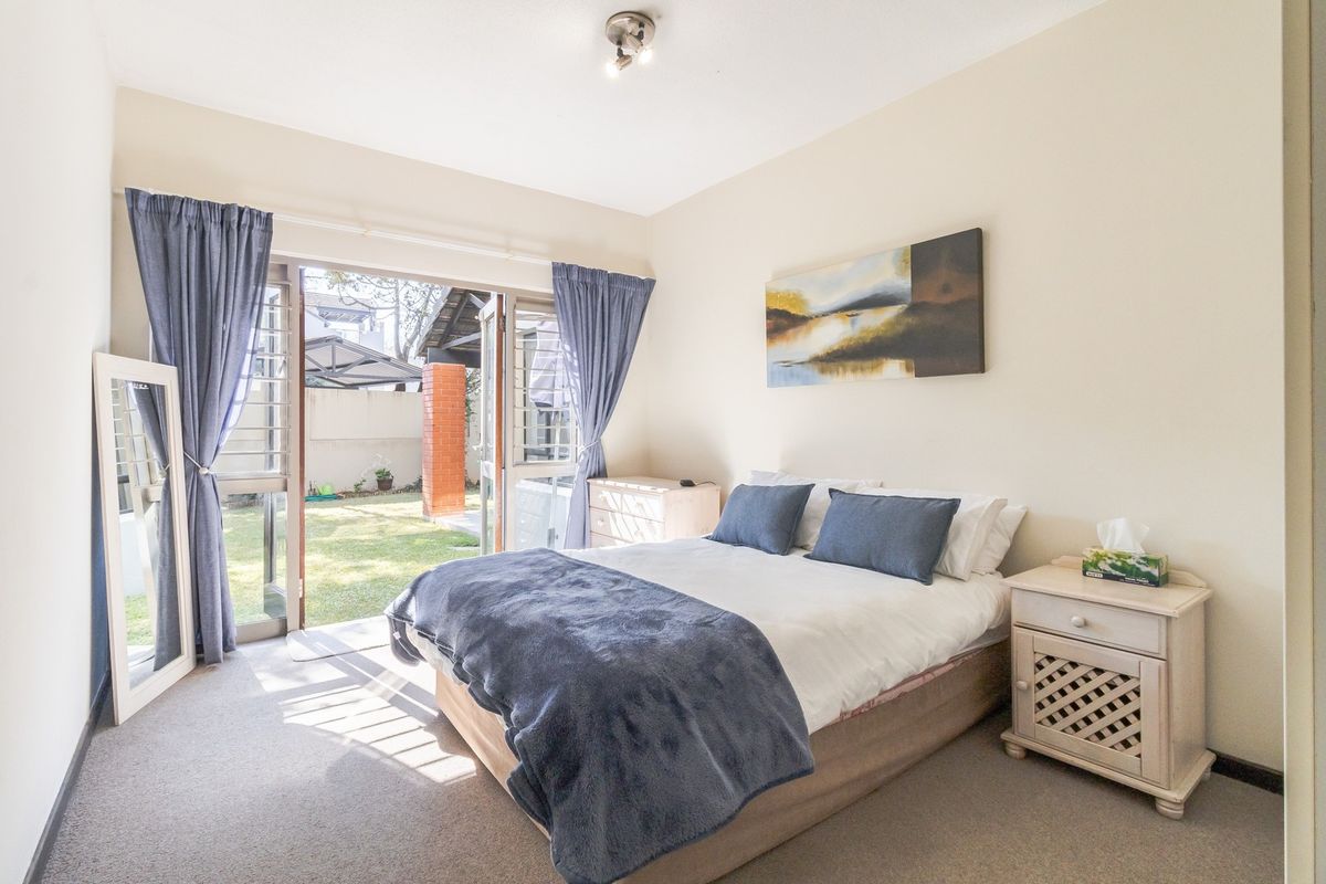 A bright bedroom featuring carpeted flooring and a sliding glass door providing direct access to the rear garden area.