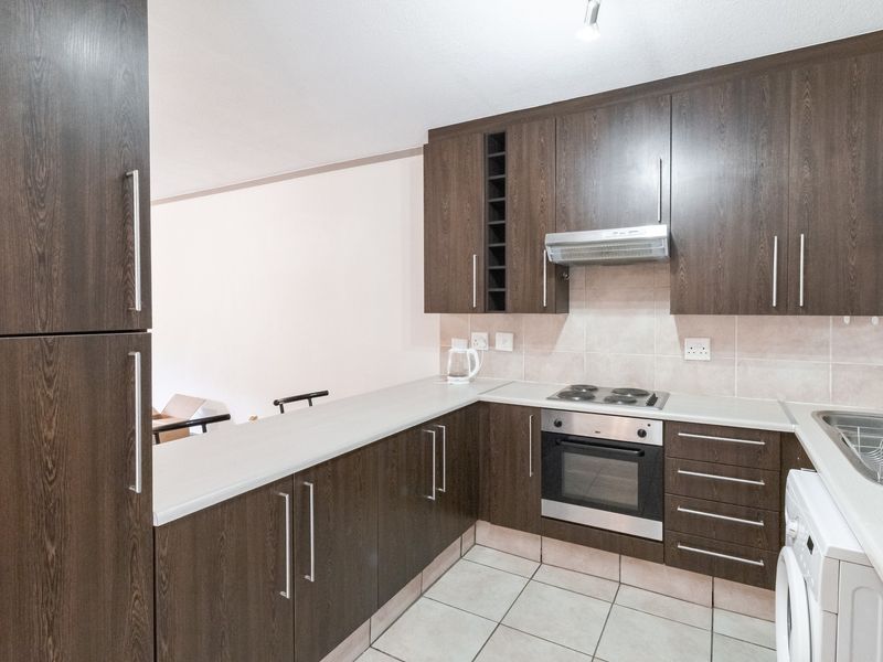 A functional kitchen featuring dark wood cabinetry, integrated oven and hob, tiled backsplash, and light-colored countertops, offering a clean and practical workspace.