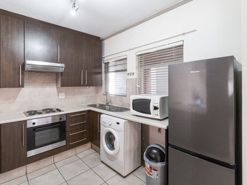 A functional kitchen featuring dark wood cabinetry, built-in oven, electric hob, extractor fan, and tiled finishes with integrated laundry plumbing.