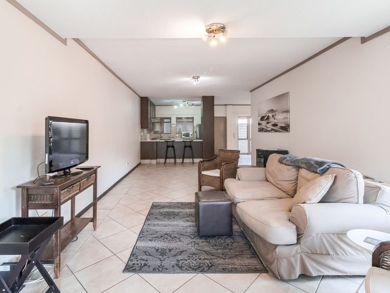 Open plan living area featuring tiled flooring and a functional kitchen with a breakfast bar, creating a seamless flow between cooking and relaxation spaces.