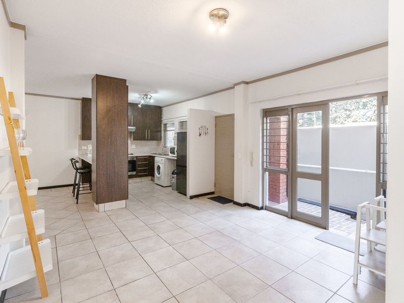 Open-plan living and kitchen area featuring tiled floors, dark wood cabinetry, built-in appliances, and sliding glass doors leading to an outdoor space.