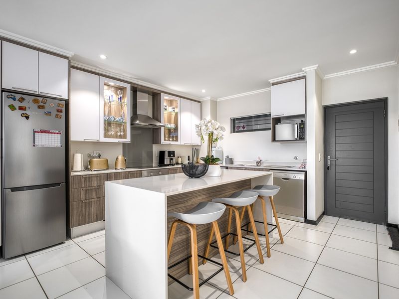 Modern kitchen featuring a central island with breakfast bar seating, sleek cabinetry, tiled flooring, and integrated appliances in a bright, open-plan layout.