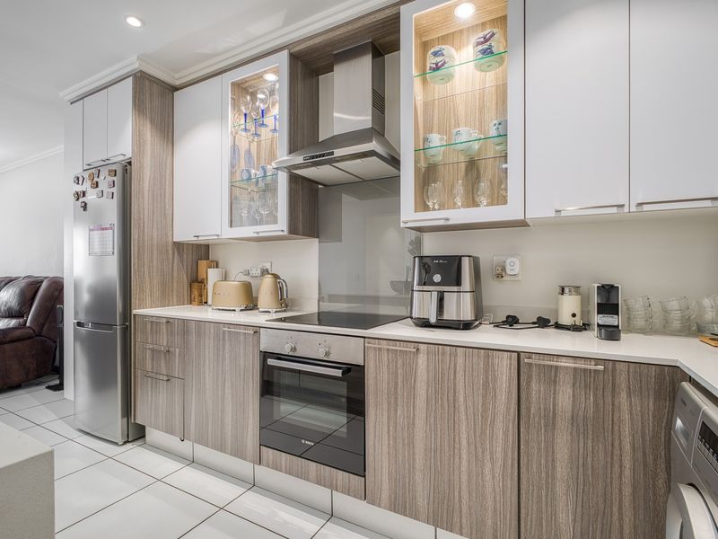 Modern kitchen featuring wood-grain and white cabinetry, stone countertops, integrated appliances, and glass-fronted display cabinets with internal lighting.