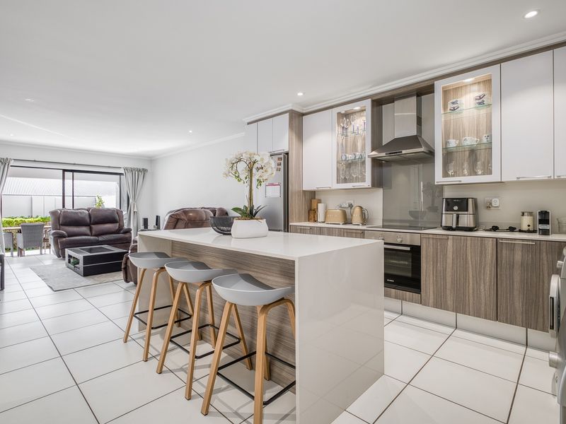 Modern open-plan kitchen and living area featuring a central island, sleek cabinetry, built-in appliances, and tiled flooring leading to a patio.