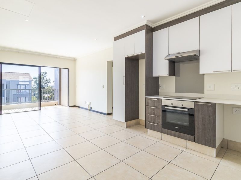 Modern open-plan kitchen and living area featuring tiled floors, built-in cabinetry with integrated appliances, and direct access to a private balcony.
