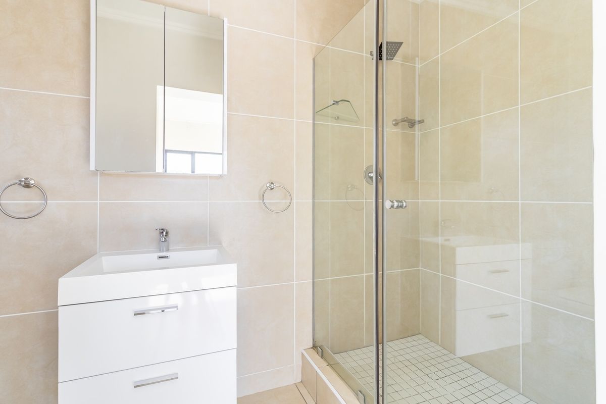 A modern bathroom featuring a white vanity cabinet, a glass-enclosed shower, and neutral wall tiling.