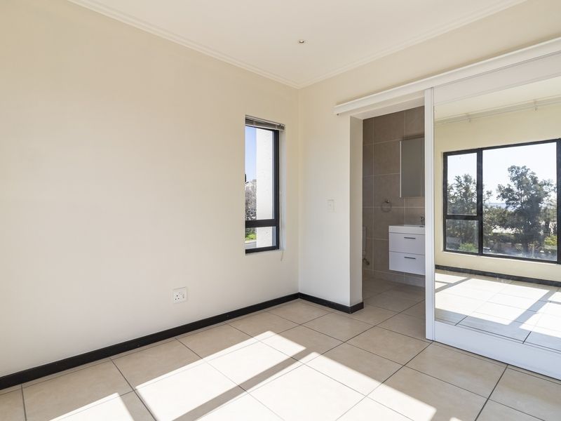 A bright, empty bedroom featuring tiled flooring, a large sliding mirror wardrobe, and direct access to an en-suite bathroom with modern finishes.