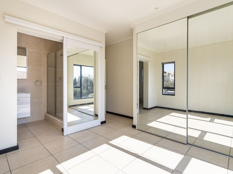 Spacious bedroom featuring large mirrored sliding wardrobes, neutral tiled flooring, and an integrated en-suite bathroom with a modern glass shower enclosure.