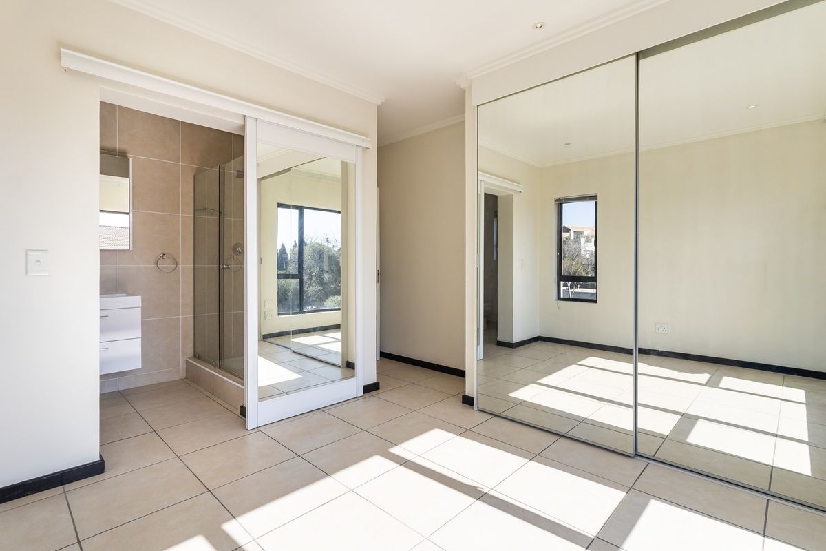 Spacious bedroom featuring large mirrored sliding wardrobes, neutral tiled flooring, and an integrated en-suite bathroom with a modern glass shower enclosure.