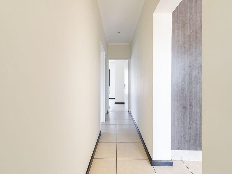 A clean, well-lit hallway featuring neutral tiled flooring, modern skirting boards, and a decorative wood-look accent wall panel.