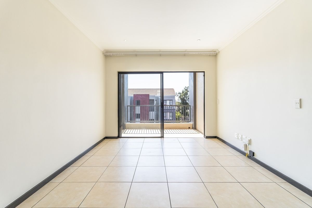 A bright, empty living room featuring neutral tiled flooring, recessed lighting, and a sliding glass door leading to an outdoor balcony.