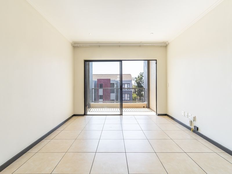 A bright, empty living room featuring neutral tiled flooring, recessed lighting, and a sliding glass door leading to an outdoor balcony.
