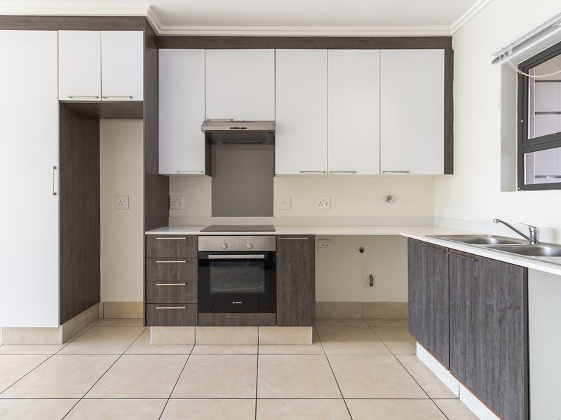 Modern kitchen featuring two-tone cabinetry, built-in oven and hob, extractor fan, and tiled flooring with ample space for appliances.