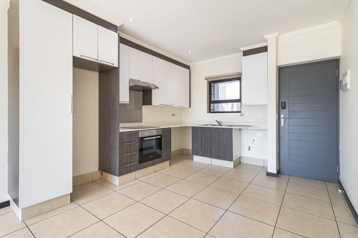Modern kitchen featuring two-tone cabinetry, built-in oven and hob, stainless steel sink, and tiled flooring, presented in a clean, empty state.