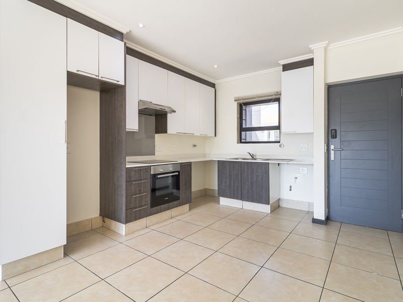 Modern kitchen featuring two-tone cabinetry, built-in oven and hob, stainless steel sink, and tiled flooring, presented in a clean, empty state.