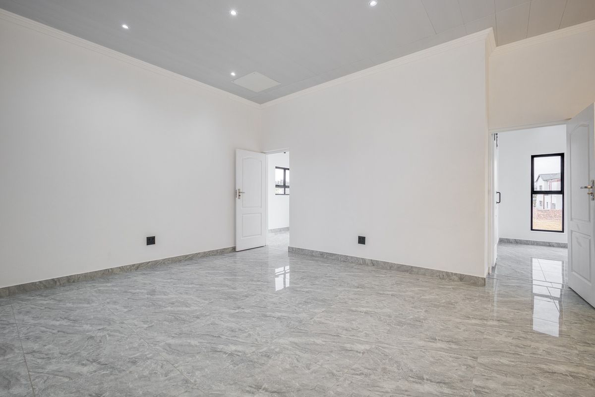 A bright, empty bedroom featuring modern grey tiled flooring, recessed downlighting, and clean white walls, offering a versatile space ready for personalization.
