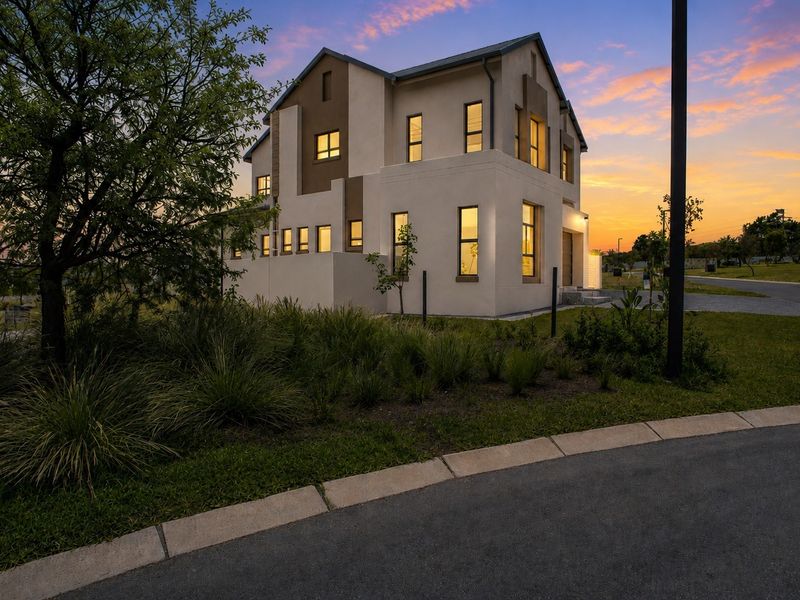 A modern two-story residential home featuring a contemporary stucco facade, pitched roof, and landscaped surroundings, captured during a vibrant sunset.