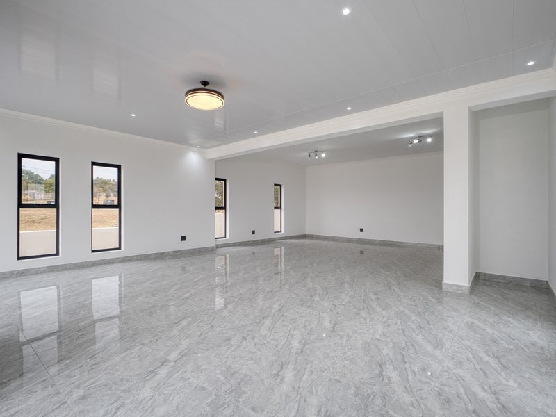 A spacious, bright open-plan living area featuring polished marble-look floor tiles, modern recessed lighting, and large black-framed windows.
