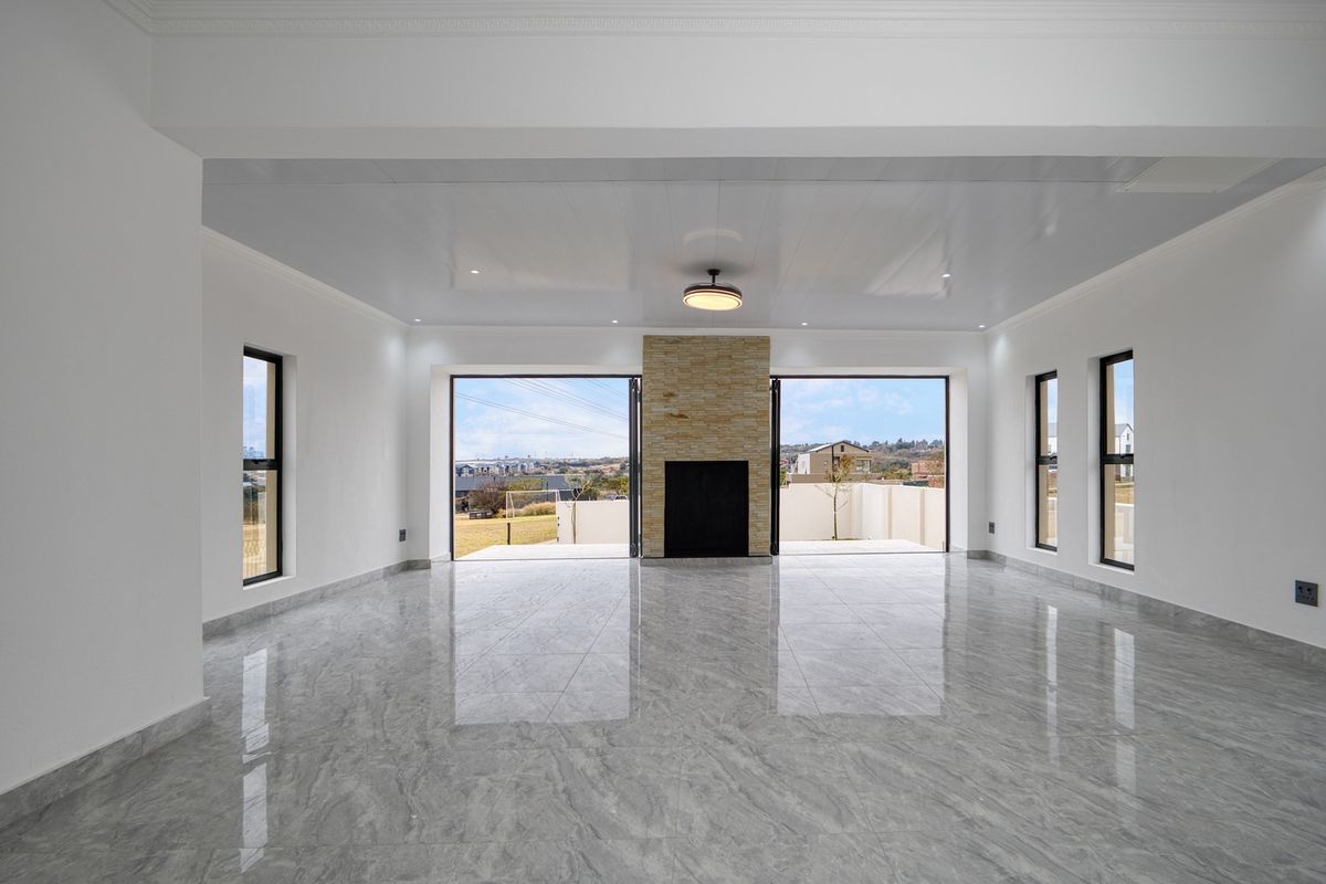 Spacious, modern living area featuring polished marble-look floor tiles, a central stone-clad fireplace, and large bi-fold doors opening to an outdoor view.