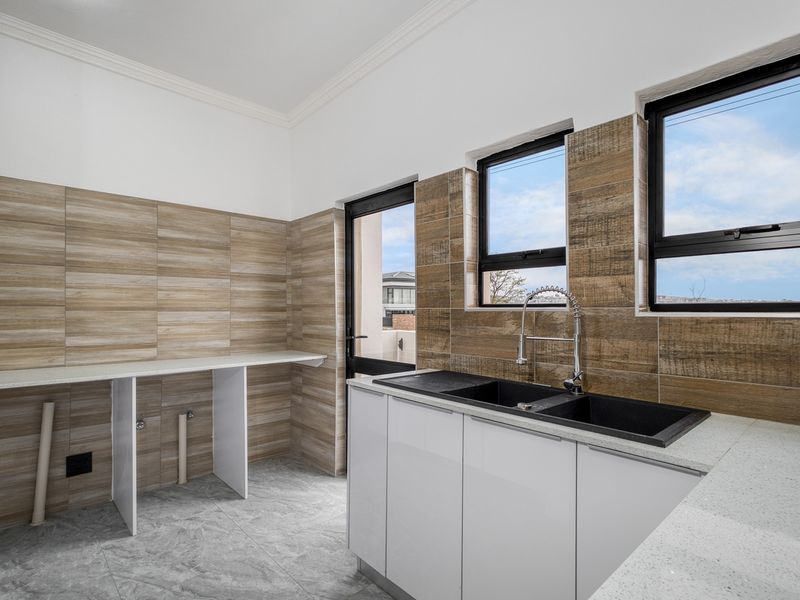 Modern scullery featuring stone countertops, double basin sink, gooseneck tap, and tiled splashback with ample space for laundry or kitchen appliances.