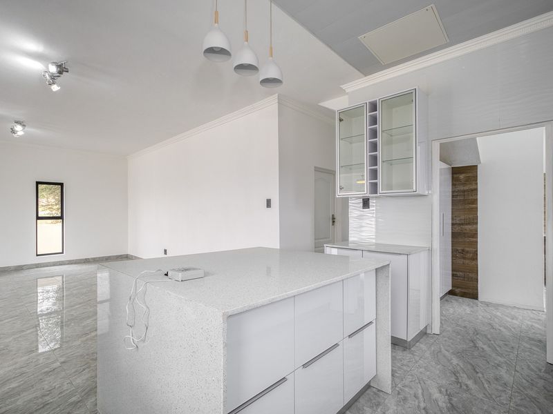Modern, bright kitchen featuring a central island with quartz countertops, sleek white cabinetry, glass-front display units, and polished tiled flooring.