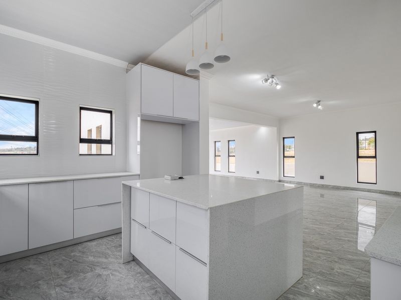 Modern open-plan kitchen and living area featuring sleek white cabinetry, quartz countertops, large format tiled flooring, and abundant natural light.