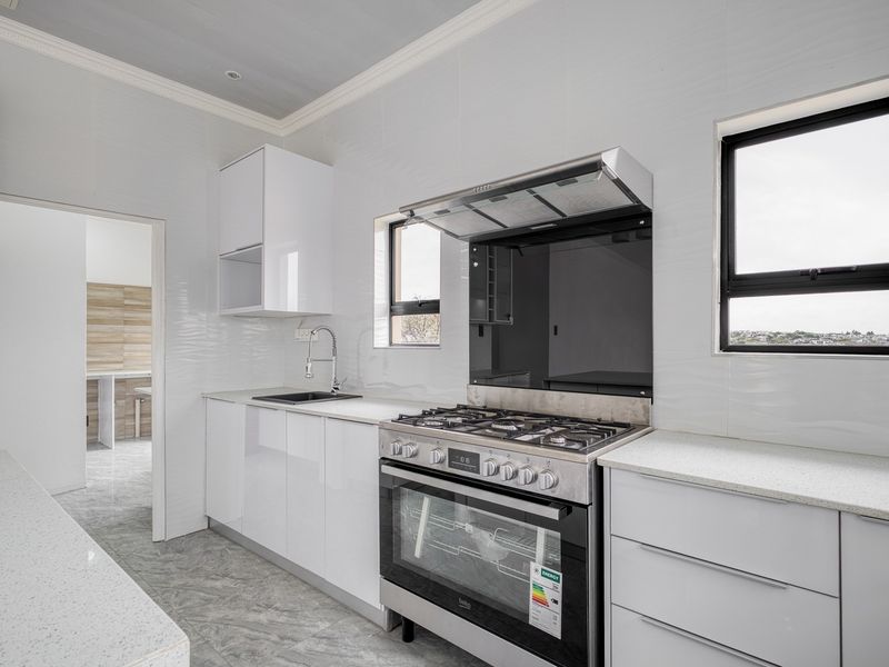Modern kitchen featuring white high-gloss cabinetry, stone countertops, a gas stove with extractor fan, and sleek tiled finishes.