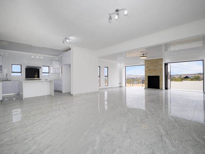 Spacious open-plan living and kitchen area featuring polished marble-look tiles, a stone fireplace, and bi-fold doors opening to an expansive outdoor view.