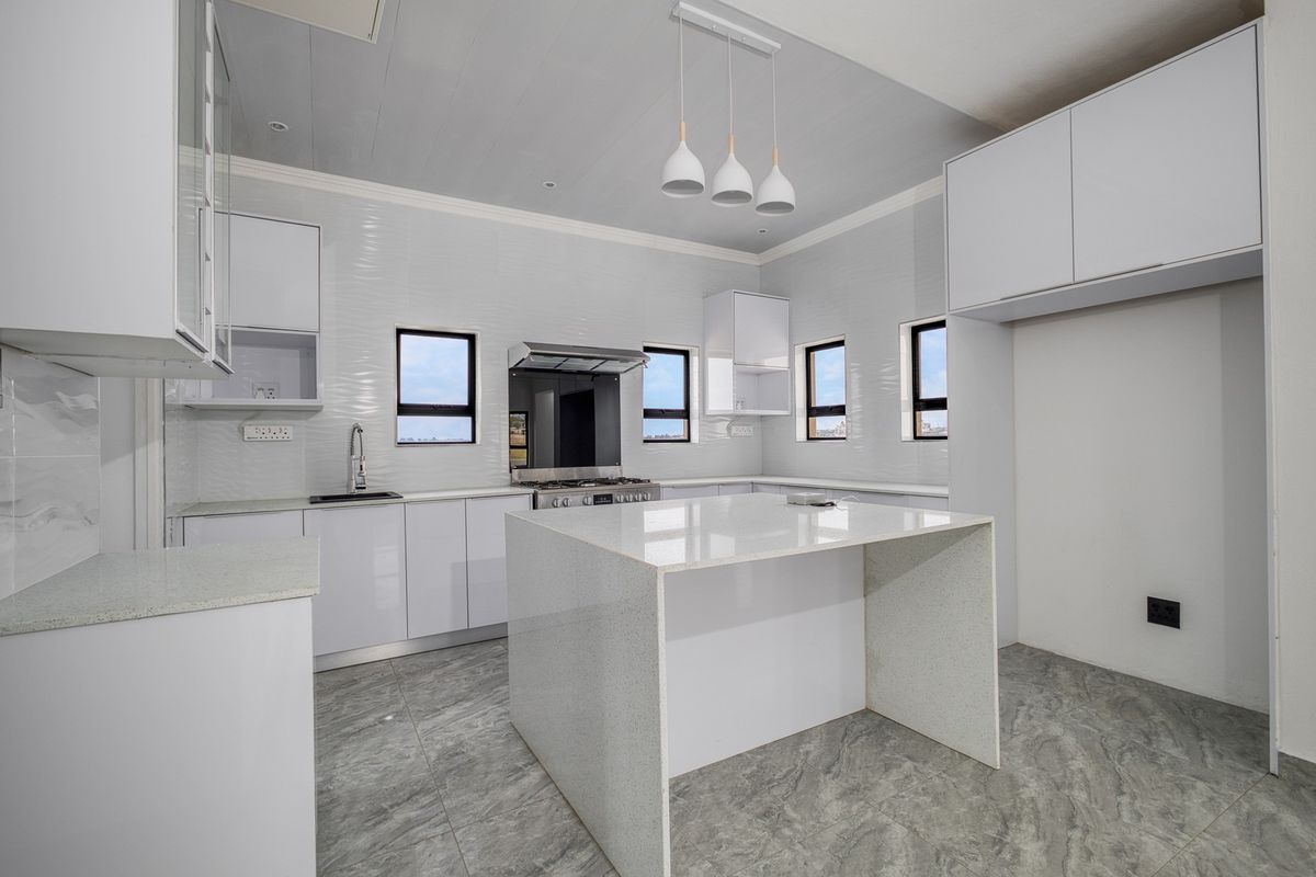 Modern kitchen featuring white cabinetry, quartz countertops, a central island, stainless steel gas stove, and contemporary pendant lighting.