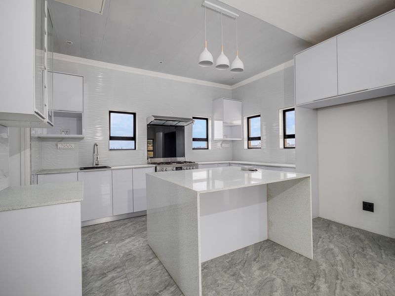Modern kitchen featuring white cabinetry, quartz countertops, a central island, stainless steel gas stove, and contemporary pendant lighting.