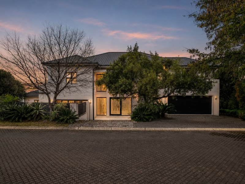A well-maintained two-story residential property featuring a paved driveway, double garage, and established garden at dusk.