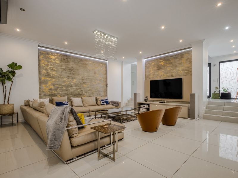 Spacious modern living room featuring high-gloss porcelain tiles, recessed downlighting, and elegant metallic feature walls with integrated media cabinetry.