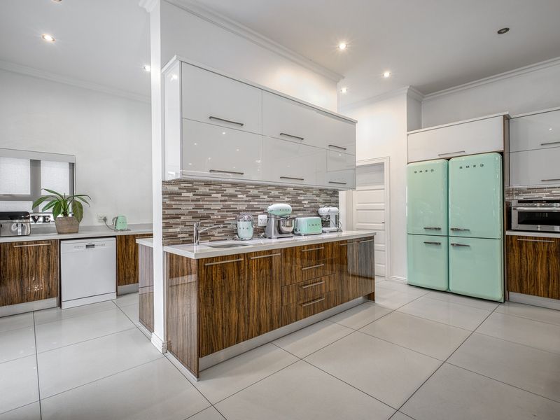 Modern kitchen featuring high-gloss wood veneer cabinetry, stone countertops, mosaic backsplash, and integrated appliances with a bright, contemporary finish.