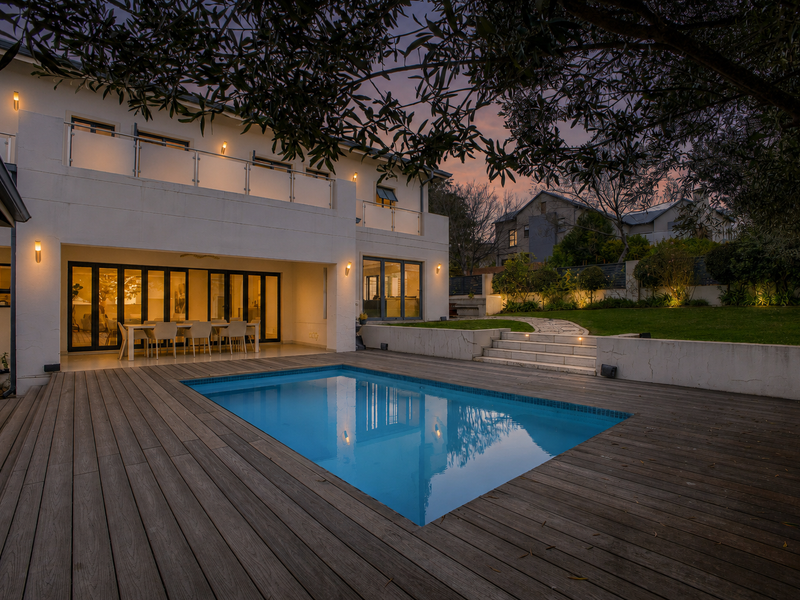 A beautifully landscaped rear exterior featuring a swimming pool, timber decking, and a spacious patio area with bi-fold doors leading into the home.