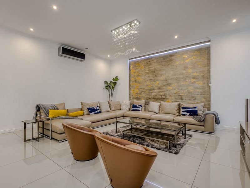 A modern, well-maintained living room featuring polished tiled floors, a decorative feature wall, recessed lighting, and a wall-mounted air conditioning unit.