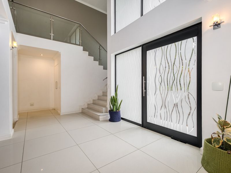 Spacious double-volume entrance hall featuring large format floor tiles, a modern staircase with glass balustrade, and a striking frosted glass front door.
