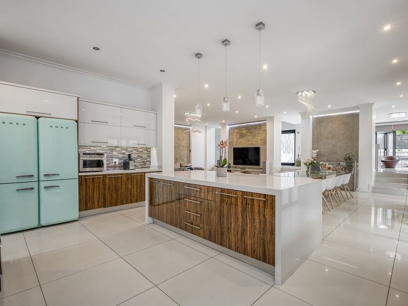 Modern open-plan kitchen and living area featuring a large central island, high-gloss cabinetry, stone countertops, and premium integrated appliances with polished tile flooring.