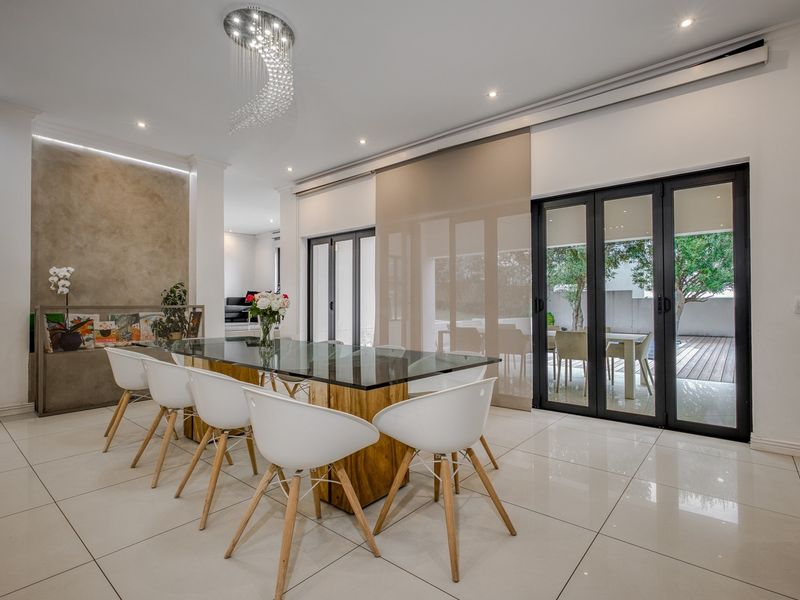 Modern dining room featuring polished porcelain tiles, a striking crystal chandelier, and black aluminium stacker doors opening to an outdoor patio area.