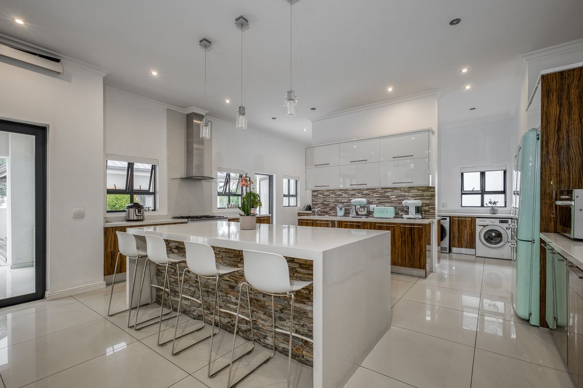 Modern open-plan kitchen featuring a large stone-clad island, glossy cabinetry, stone countertops, and integrated laundry facilities with high-quality finishes.