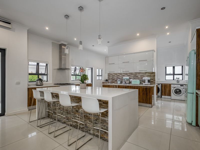 Modern open-plan kitchen featuring a large stone-clad island, glossy cabinetry, stone countertops, and integrated laundry facilities with high-quality finishes.