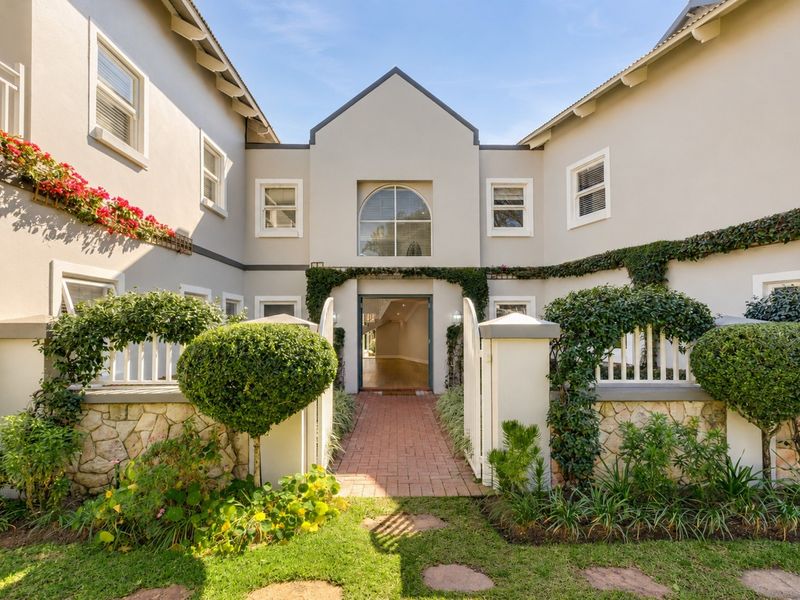 A charming front entrance featuring a brick paved walkway, stone-clad boundary walls, white picket fencing, and manicured garden beds leading to the main residence.