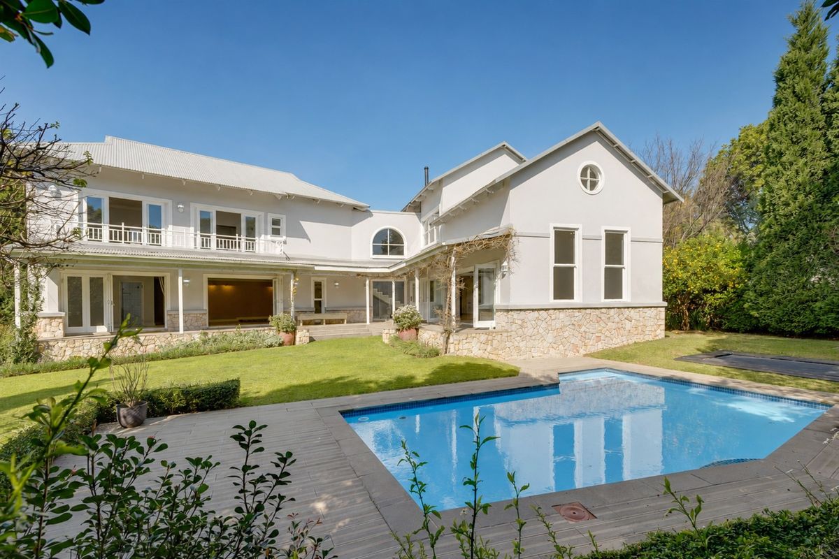 Rear view of a spacious two-story house featuring a swimming pool, stone-clad base, metal roof, and a well-maintained garden with a deck area.